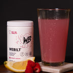 WeBilt electrolyte container with a glass of  it mixed in water and lemon and raspberry slices on a dark background