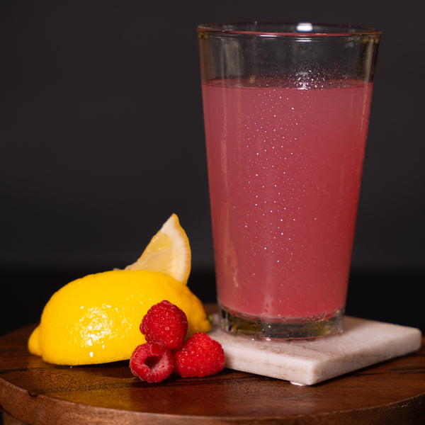 Electrolyte drink in a glass with lemon and raspberries on a dark background