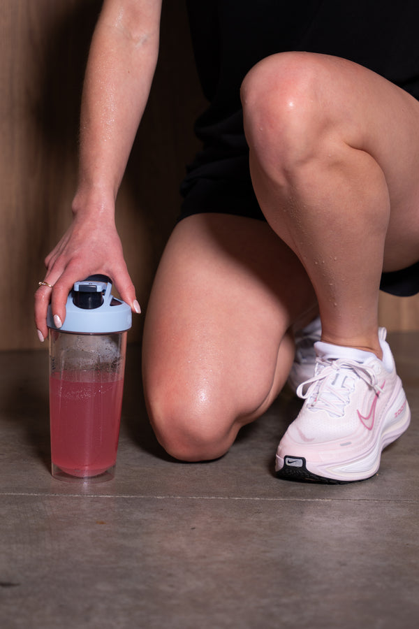 Person holding a pink drink container on a concrete floor.